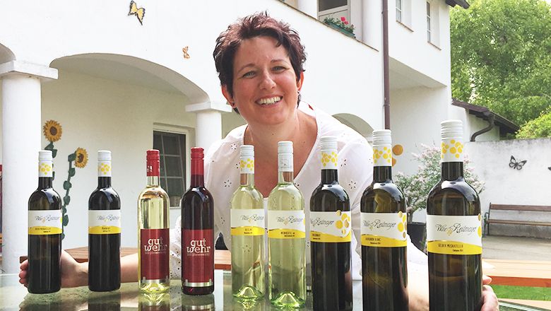 Woman presenting a selection of wine bottles on an outdoor table.