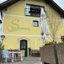Yellow building with the inscription 'Zum Stickelberg Wirtshaus', terrace with colorful chairs and parasol.