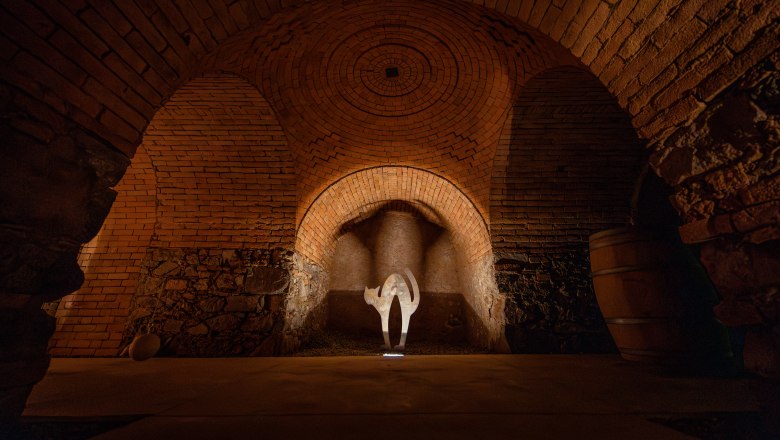 A wine cellar with brick walls and an illuminated work of art in the shape of a cat.