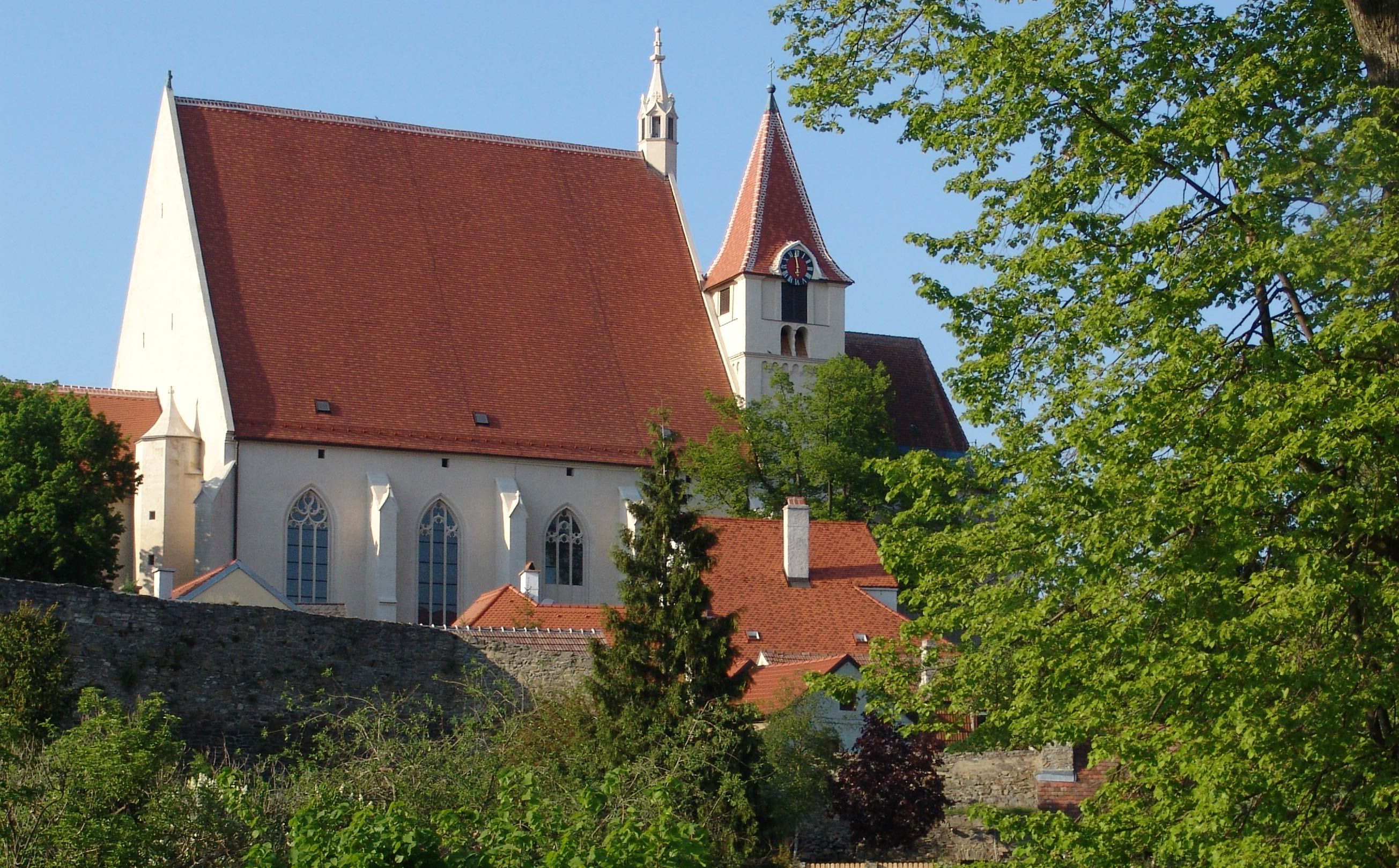 St. Stephen's parish church with red roof and tower, surrounded by trees and a stone wall.
