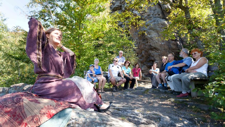 A woman in a purple robe tells a story to a group of people outside.