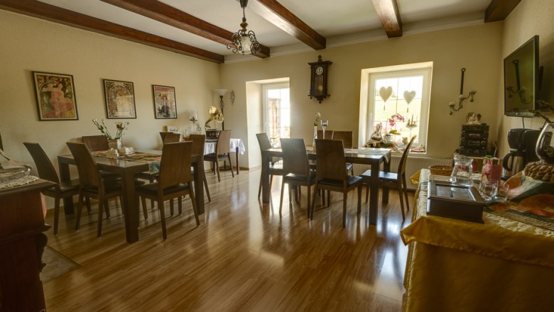 Cozy breakfast room with wooden floor, tables and chairs, decorated with pictures and a wall clock.