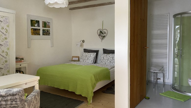 Comfortable double room with green bedspread, small desk and adjoining bathroom with shower.