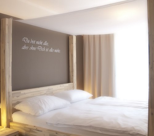 A four-poster bed in a bright room with a quote on the wall.
