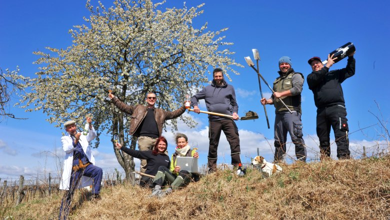 Group of people with tools and drinks in front of a blossoming tree outdoors.