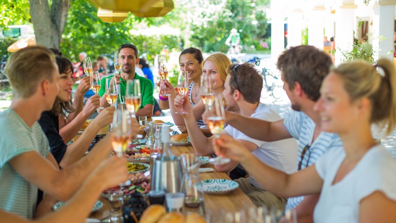 Group of people clinking glasses of wine at a long outdoor table.