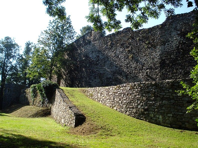 Old city wall with green area and trees in the sunlight.