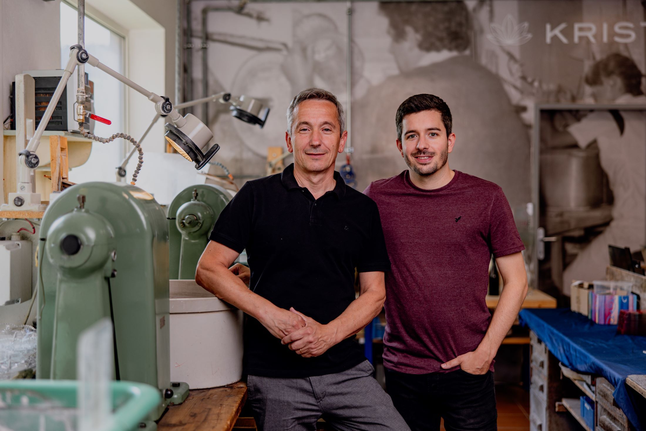 Two men are standing in a workshop with machines in the background.
