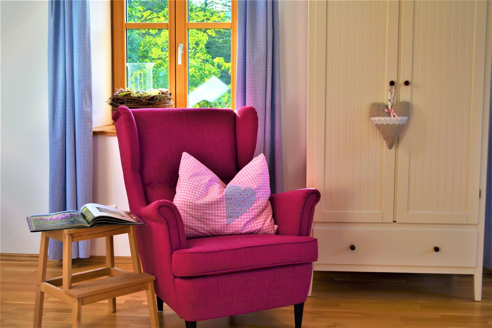Cozy room with pink armchair, cushions, small table and wardrobe.