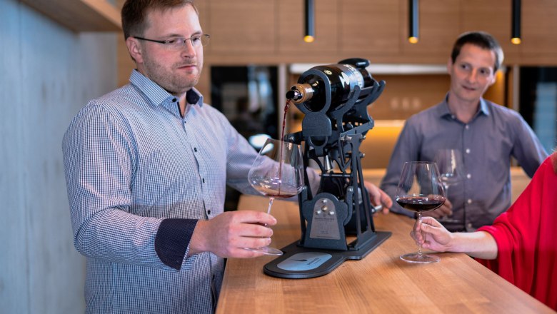 Two men and a woman at a wine tasting in a modern winery.