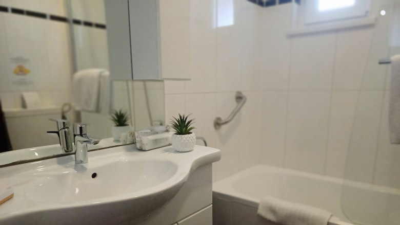 Bathroom with washbasin, mirror, bathtub and towel.
