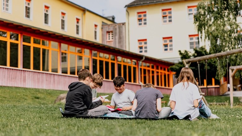 Group of children sitting on a meadow in front of a yellow building.