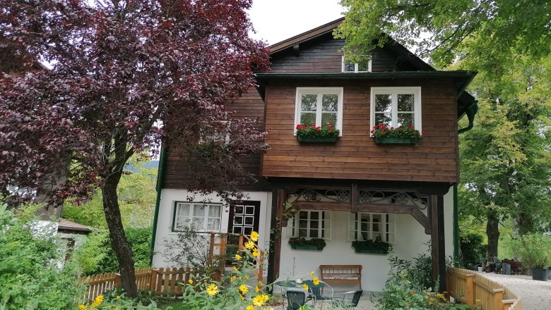 A two-story wooden house with flower boxes and garden.