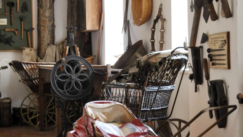 A room in a local history museum with antique objects such as a red baby carriage, tools and stuffed birds on the walls.
