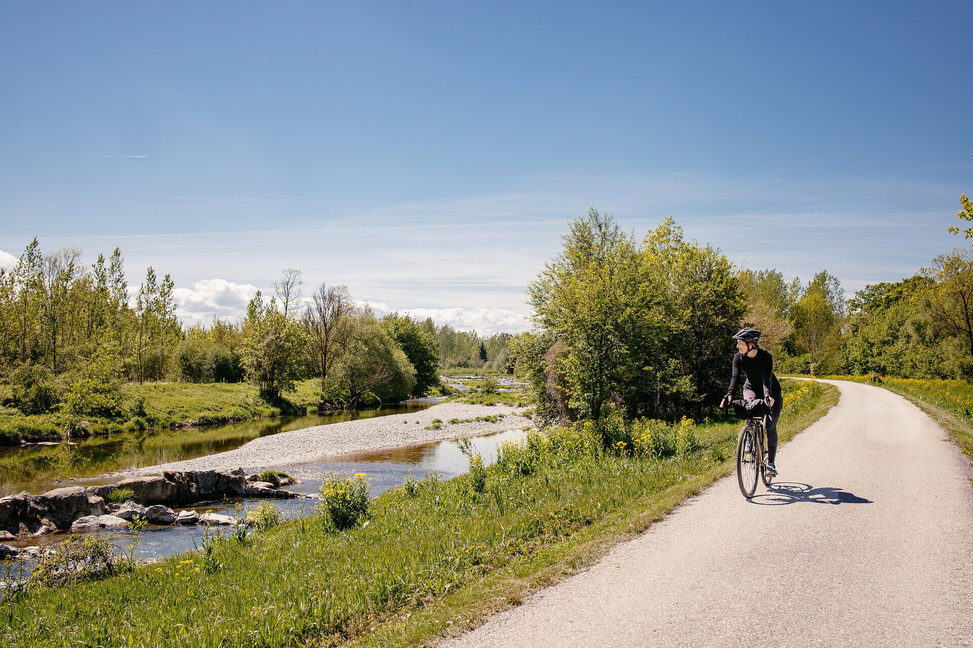 A picturesque cycle path meanders along a gently babbling brook, surrounded by lush greenery and flowering meadows. The clear air and bright sunshine invite you to enjoy the beauty of nature and unwind.