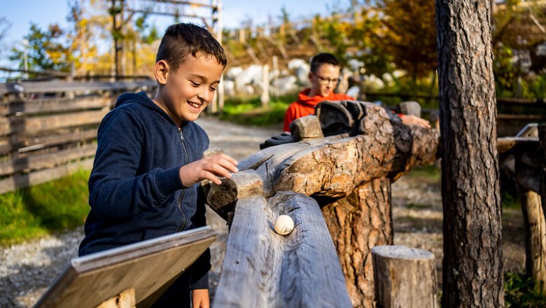 Two boys playing on a wooden ball track outdoors.