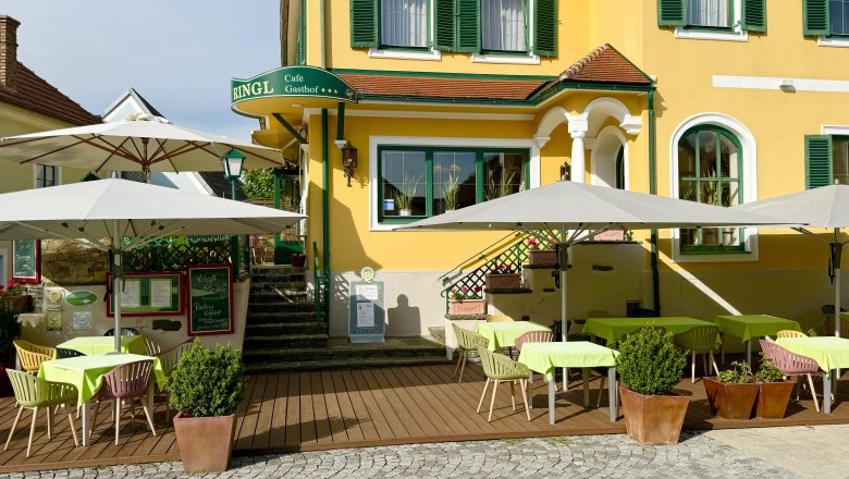 A yellow building with green shutters and a garden with tables and parasols.