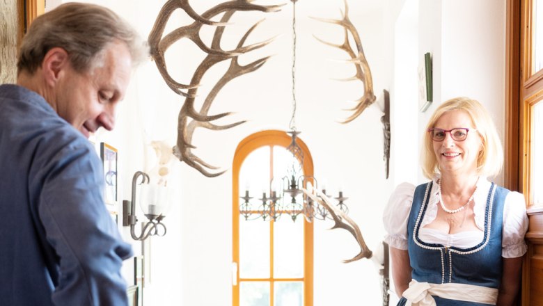 A man and a woman in traditional dress stand in a hallway with antlers on the wall.