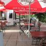 An empty guest garden with wooden tables and chairs under red parasols.
