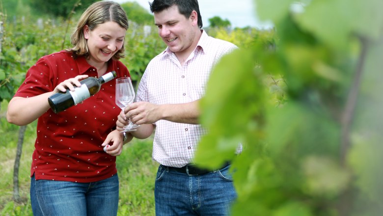 Two people in the vineyard, a woman pouring wine into a glass.