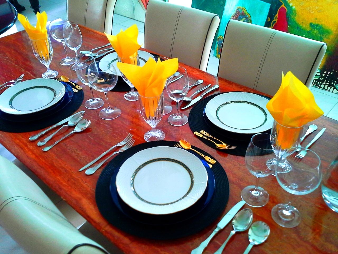 Elegant dining table with crockery, cutlery and yellow napkins.