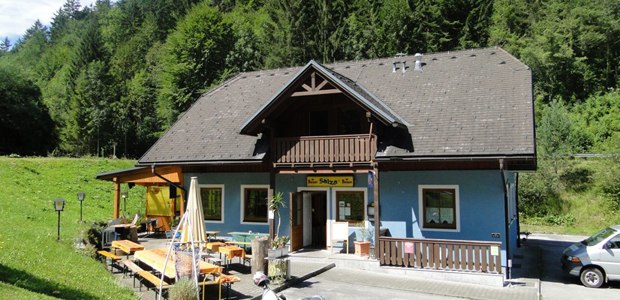 A blue building with a wooden balcony and terrace, surrounded by trees.