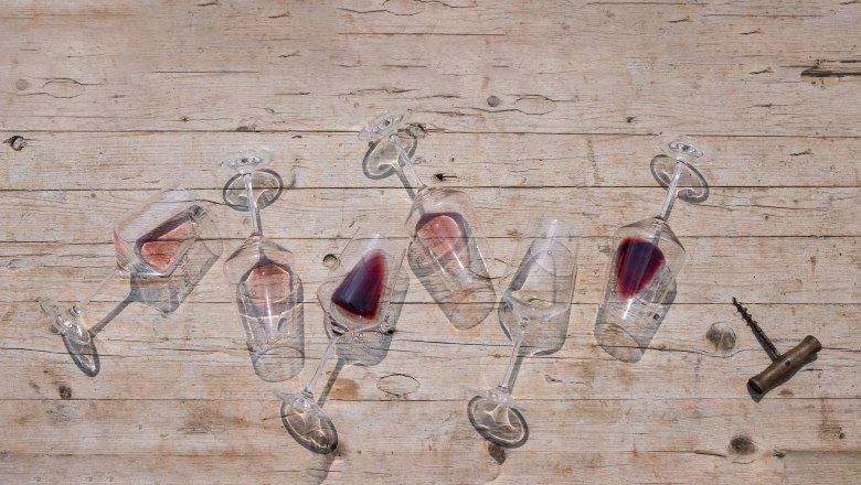 Six overturned wine glasses with red wine on a wooden table, a corkscrew next to them.