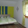 Bedroom with double bed, green and yellow striped wall, green curtains, wooden floor.