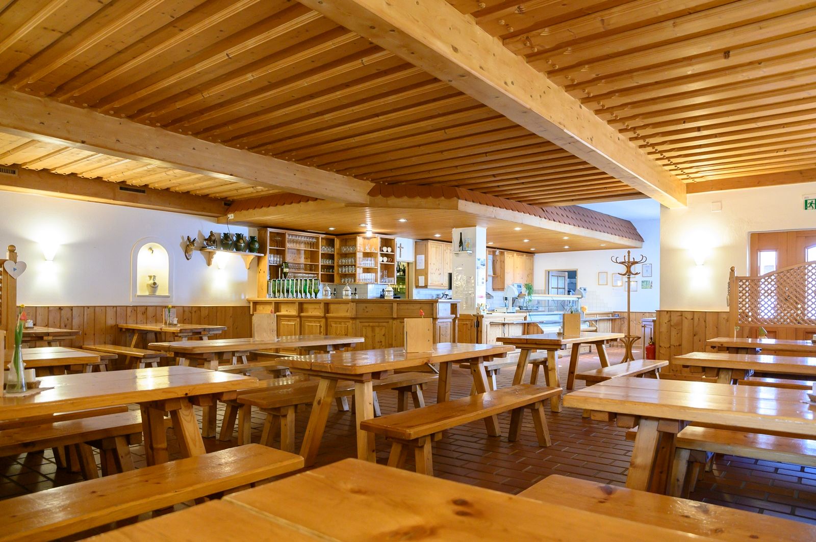 Interior view of a rustic dining room with wooden tables and benches, a bar and decorative elements on the walls.