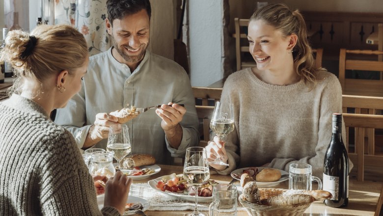 Three people sit at a table in a cozy restaurant and enjoy wine and food.