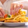 A plate with Wiener Schnitzel, French fries, lemon and tomato is served by one person.