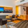 Modern hotel suite with sofa, armchair, TV and kitchenette.