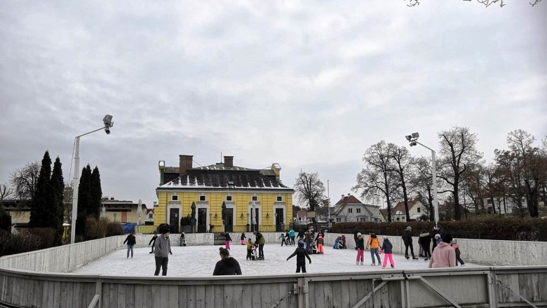 People skating on an open-air rink in front of a yellow building.