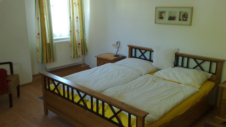 Bedroom with double bed, yellow bed linen, wooden furniture and floral curtains.