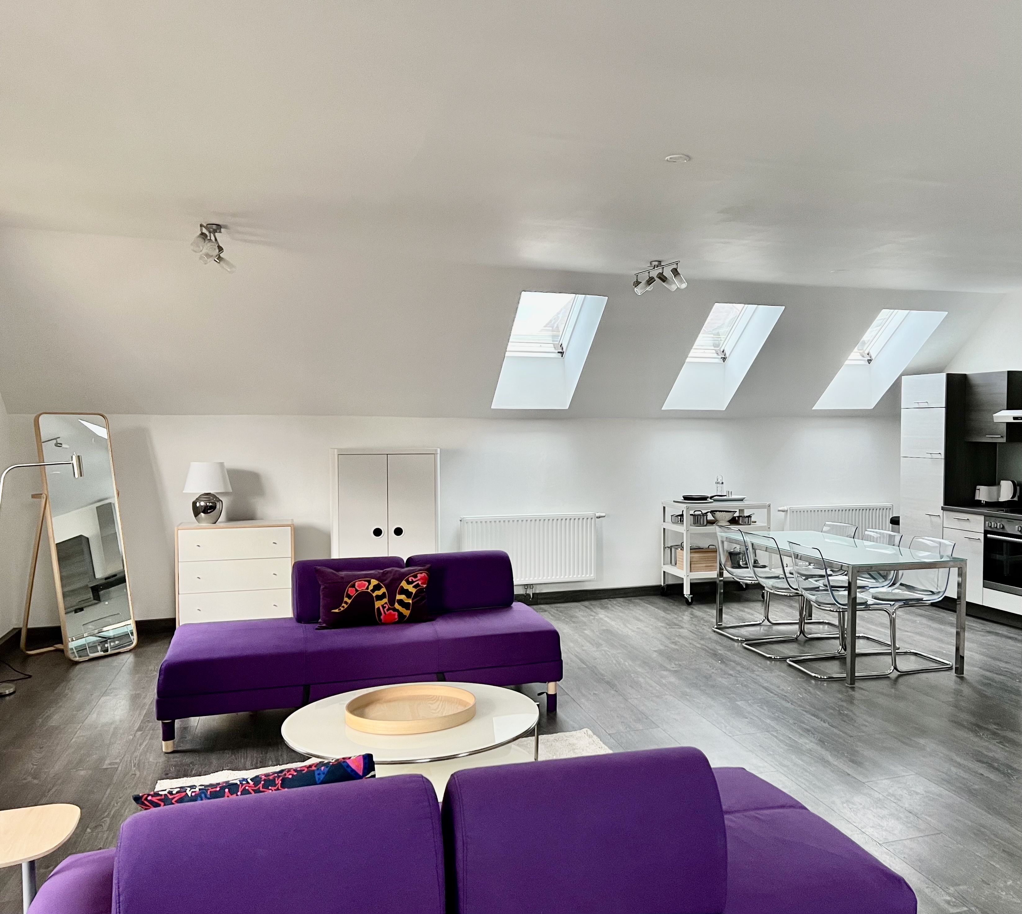 Modern loft with purple sofas, dining table and kitchenette under skylights.