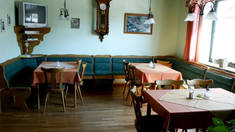A traditionally furnished breakfast room with wooden furniture, tables with orange tablecloths, a wall clock and a TV.
