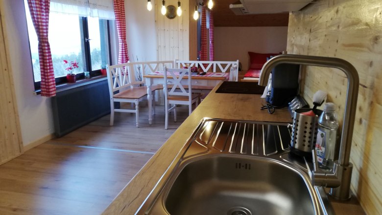 Kitchen in an attic apartment with wood paneling, sink, dining table and red curtains.
