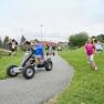 Children play on an adventure playground with Kettcars and run across a meadow.