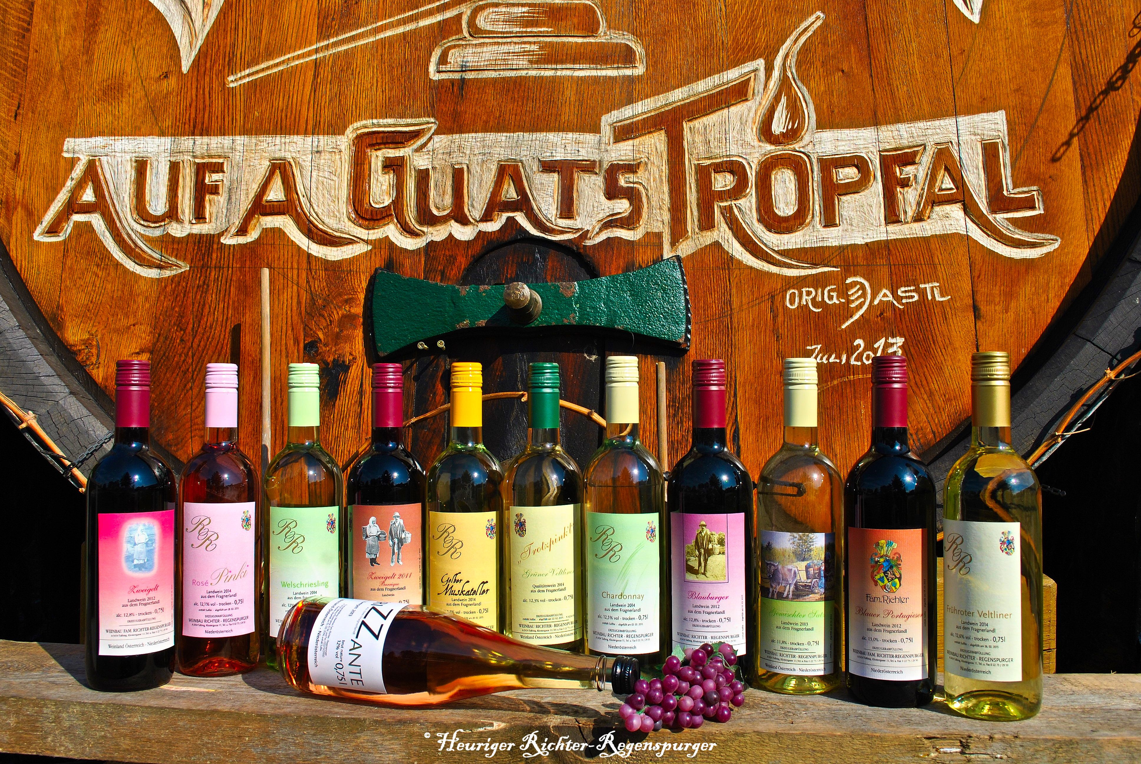 Various bottles of wine in front of a large wooden barrel with the inscription 'Auf a guats Tropfal'.