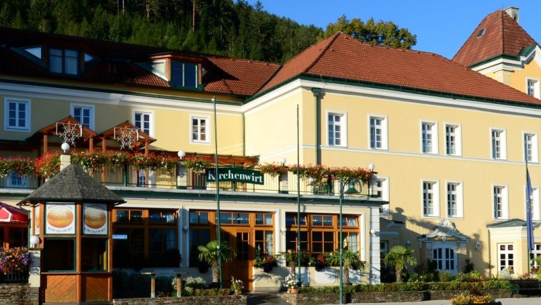 Exterior view of a yellow building with red roofs and the sign 'Kirchenwirt'.