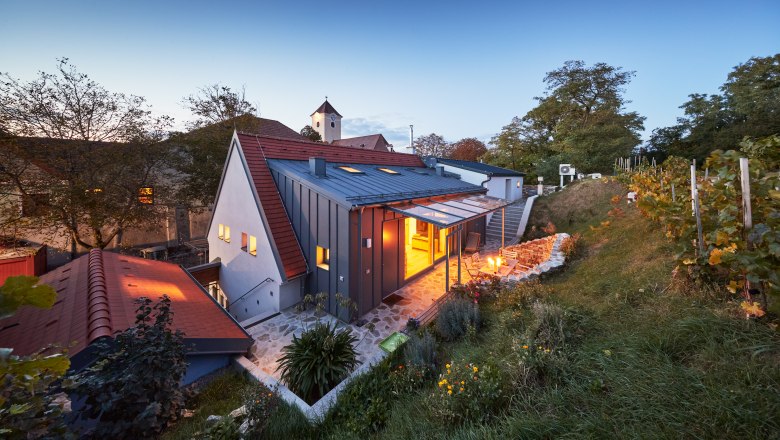 Winery with illuminated courtyard and vines in the foreground at dusk.