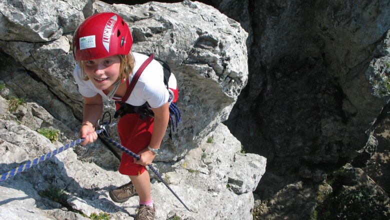 Person climbing on rocks with red helmet and rope.