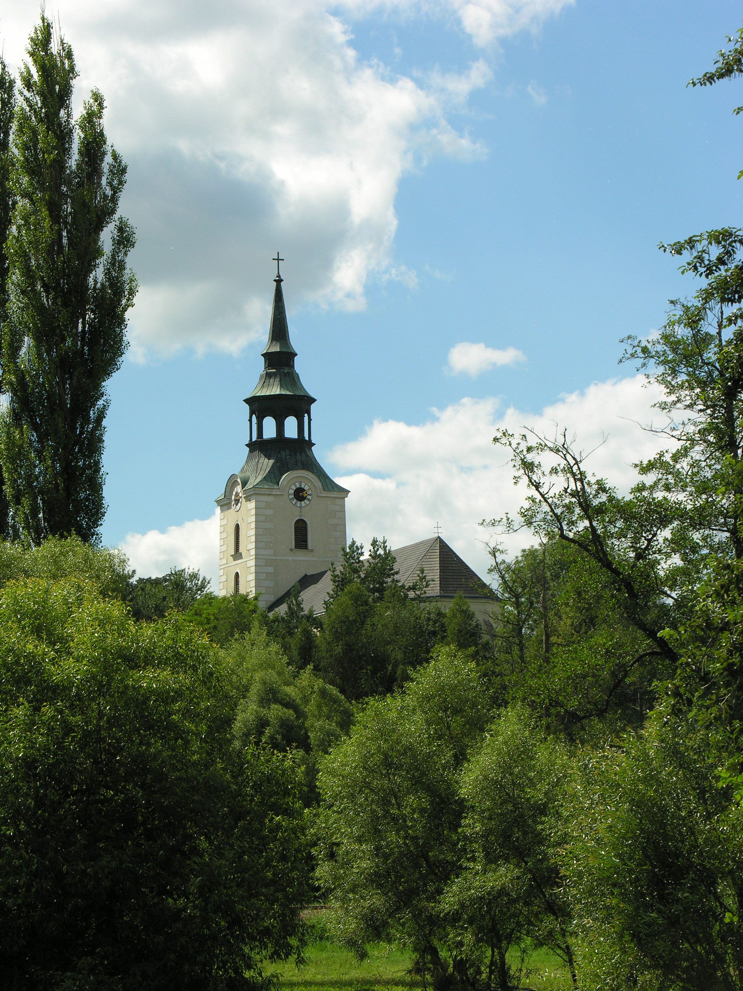 Church tower in Dobersberg surrounded by trees and blue sky.