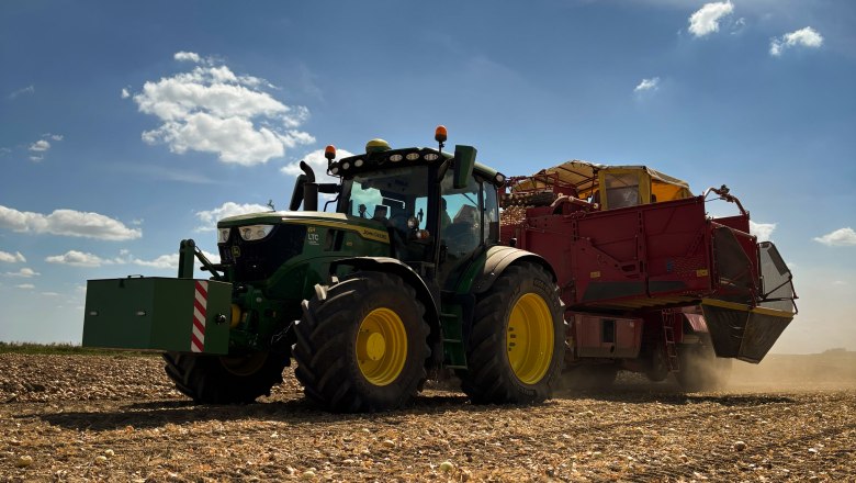 A tractor with a trailer drives across a harvested field under a blue sky with a few clouds.