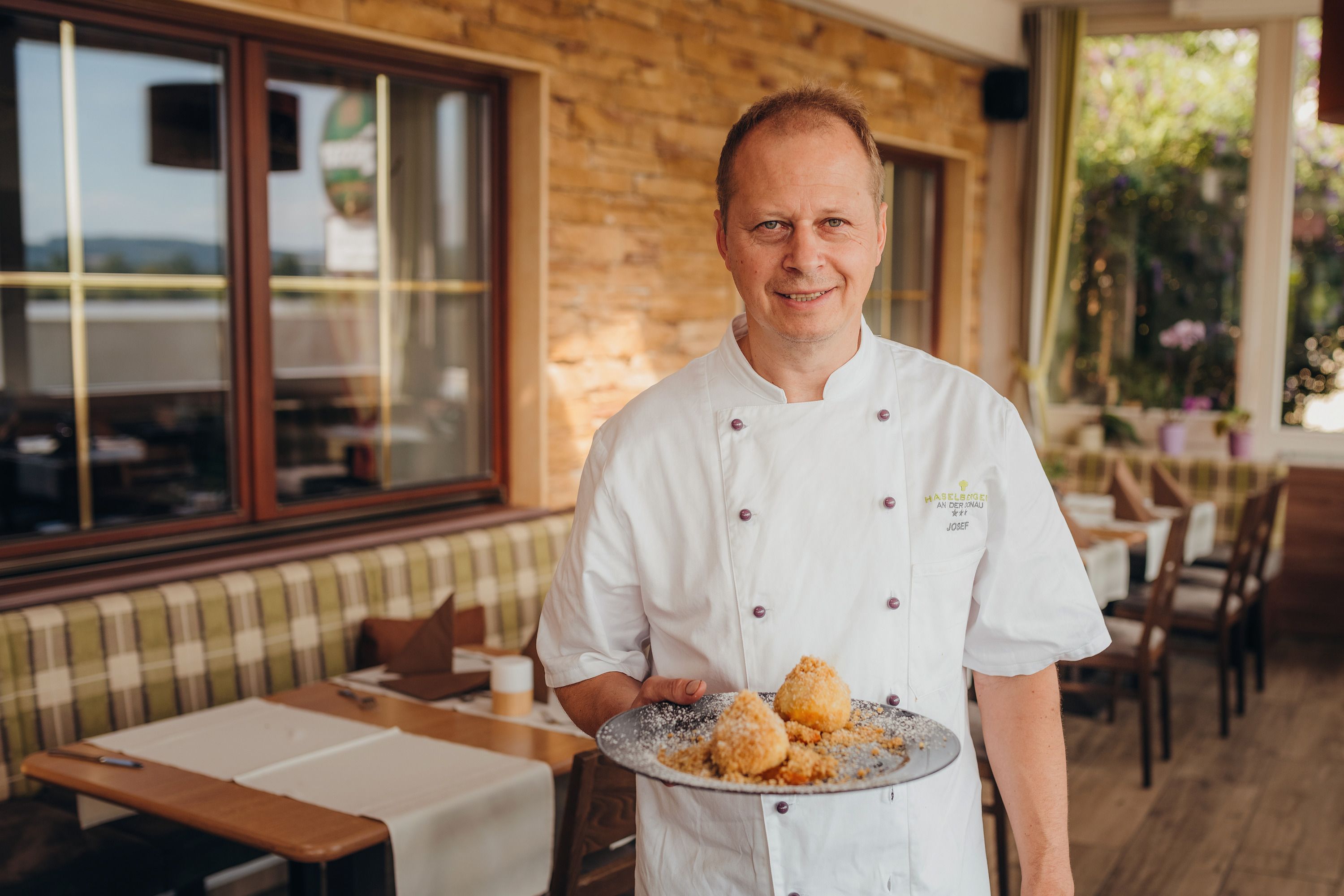 Cook in white uniform presenting plates of dumplings in a restaurant.