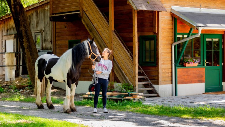 A woman stands next to a black and white horse in front of a wooden building.