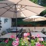 Cozy outdoor area with tables, chairs and parasols, surrounded by flowers and plants.