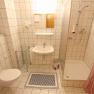 Small bathroom with shower, washbasin and toilet, tiled in white.