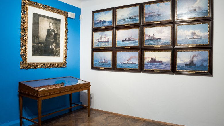 A museum room with maritime paintings and a portrait on the wall.