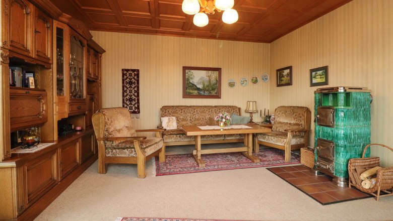 Cozy living room with wooden furniture, green tiled stove and carpet.